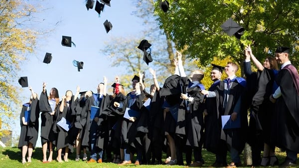 Los graduados del Cheltenham College lanzan sus birretes al aire frente a árboles verdes.