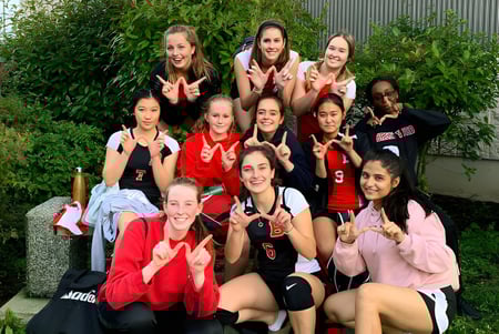 Un grupo de estudiantes de la Chemainus Secondary School está al aire libre en ropa deportiva y hace gestos con las manos frente a un fondo verde.