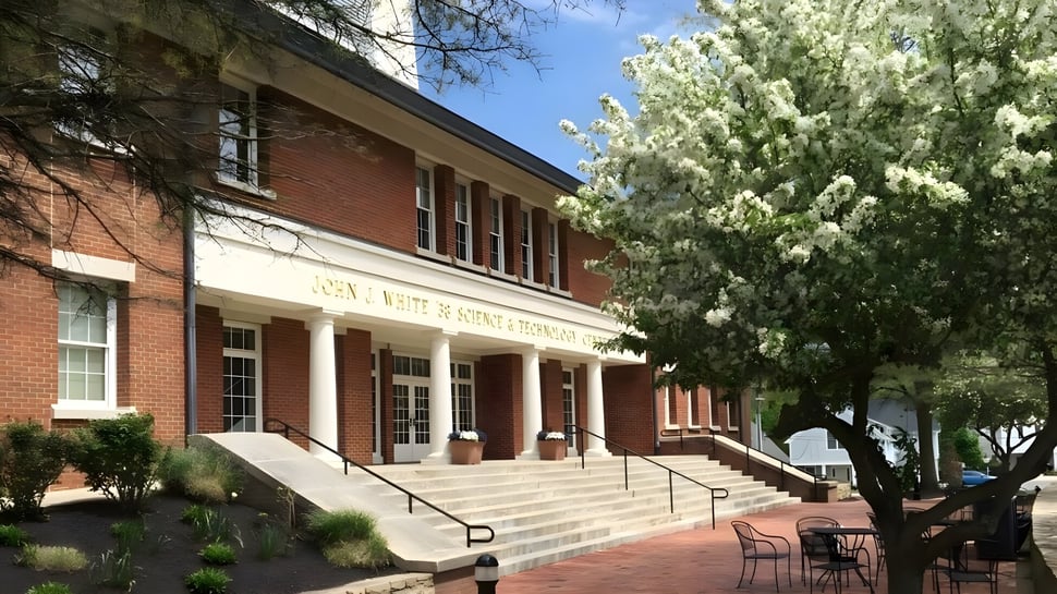 El edificio de ladrillo con entrada de columnas en el campus de la Cheshire Academy está rodeado de árboles en flor y un camino pavimentado.