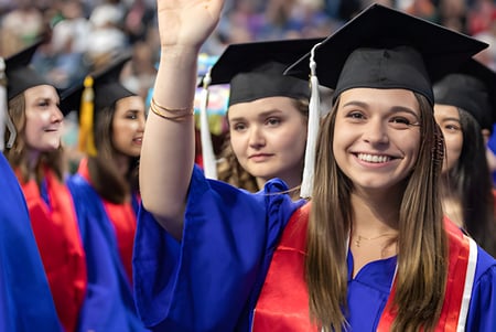 Un grupo de graduadas y graduados de Chicago Public Schools se encuentra juntos en sus togas de graduación azules y rojas.