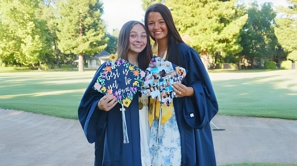 Dos estudiantes en coloridos trajes de graduación están en el parque del Chico Unified School District y sonríen juntas.