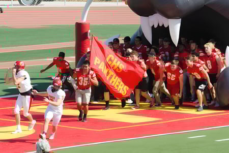 Un grupo de estudiantes en uniformes rojos con una gran bandera roja en el campo de deportes del Chico Unified School District.