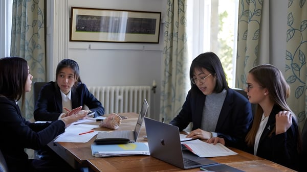 Un grupo de personas trabaja conjuntamente en una computadora portátil y documentos en una sala de reuniones de la Chigwell School.
