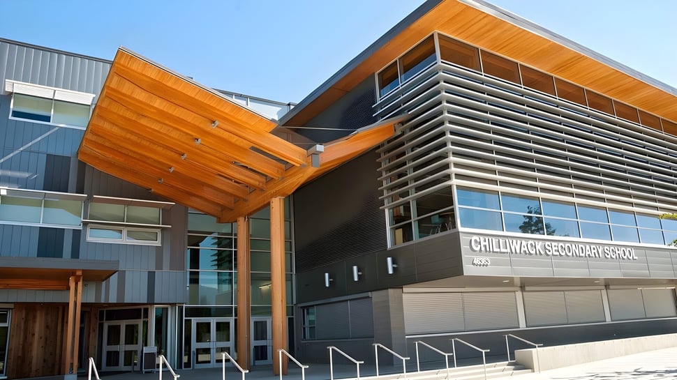 El moderno edificio de varios pisos de la Chilliwack Secondary School con fachada naranja-gris y grandes ventanales de vidrio bajo un cielo azul.