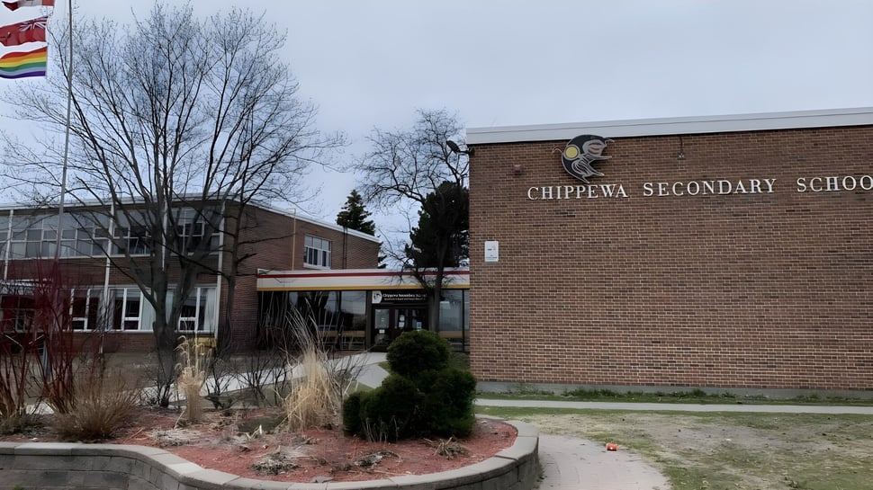 El edificio de ladrillo de la Chippewa Secondary School con la fachada etiquetada rodeado de árboles desnudos y un campo.