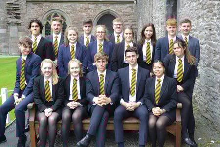 Un grupo de alumnos en uniforme está frente al edificio de piedra histórico de Christ College y posan para una foto.