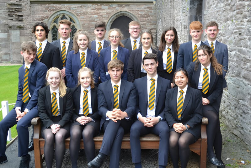 Un grupo de alumnos en uniforme está frente al edificio de piedra histórico de Christ College y posan para una foto.