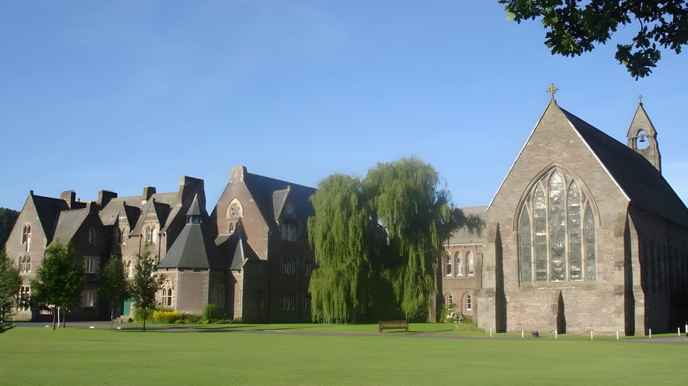 El campus de Christ College muestra un cuidado césped verde y varios edificios históricos en estilo gótico bajo un cielo despejado.