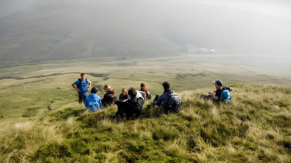 Un grupo de alumnos de Christ College está en una pradera montañosa frente a montañas envueltas en niebla.