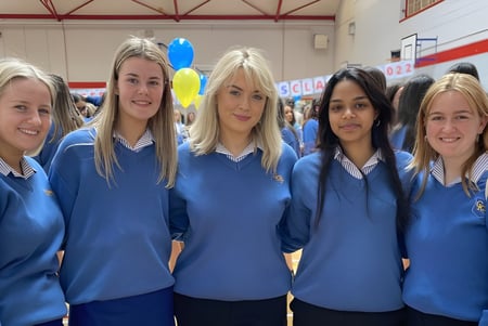 Cinco estudiantes de la Christ King Secondary School están juntos en un pasillo con globos de colores de fondo.