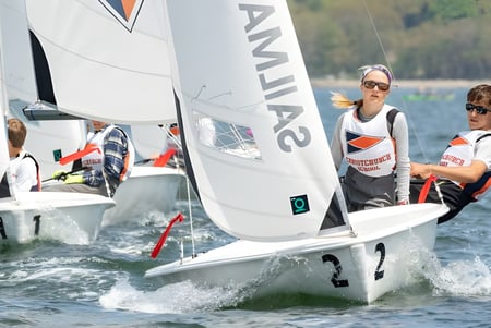 Dos estudiantes de la Christchurch School navegan en un pequeño bote en un lago con un fondo boscoso.