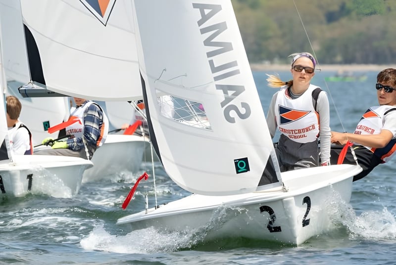 Dos estudiantes de la Christchurch School navegan en un pequeño bote en un lago con un fondo boscoso.