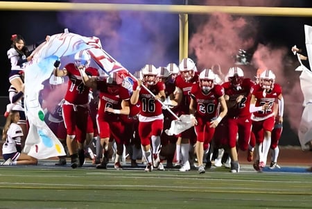 Un grupo de jugadores de fútbol en uniformes rojos está en el campo durante un evento en las Christian Unified Schools.