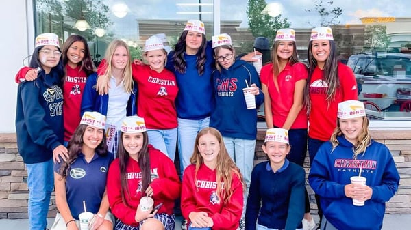 Un grupo de estudiantes de las Christian Unified Schools lleva uniformes deportivos y gorras frente a un edificio escolar.