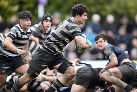 Estudiantes del Christ's College juegan un intenso partido de rugby en un campo cubierto de hierba frente a aficionados que observan.