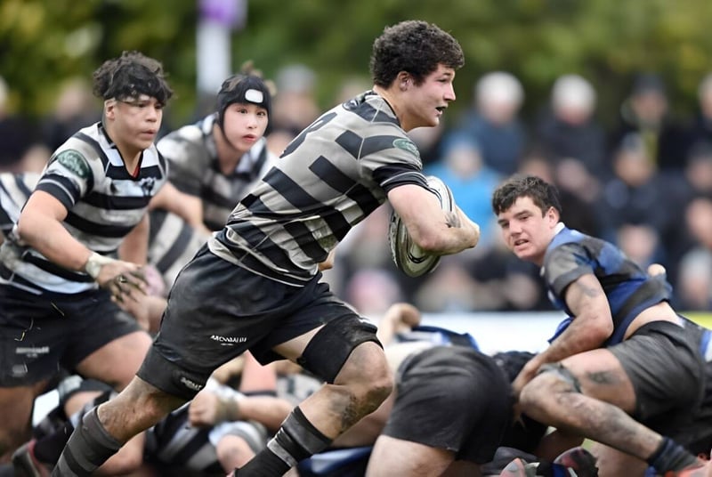 Estudiantes de Christ's College juegan un intenso partido de rugby en un campo verde frente a una tribuna.