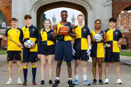 Un grupo de jóvenes deportistas de la Christ's Hospital School está frente a un edificio histórico de ladrillo con varios equipos deportivos.