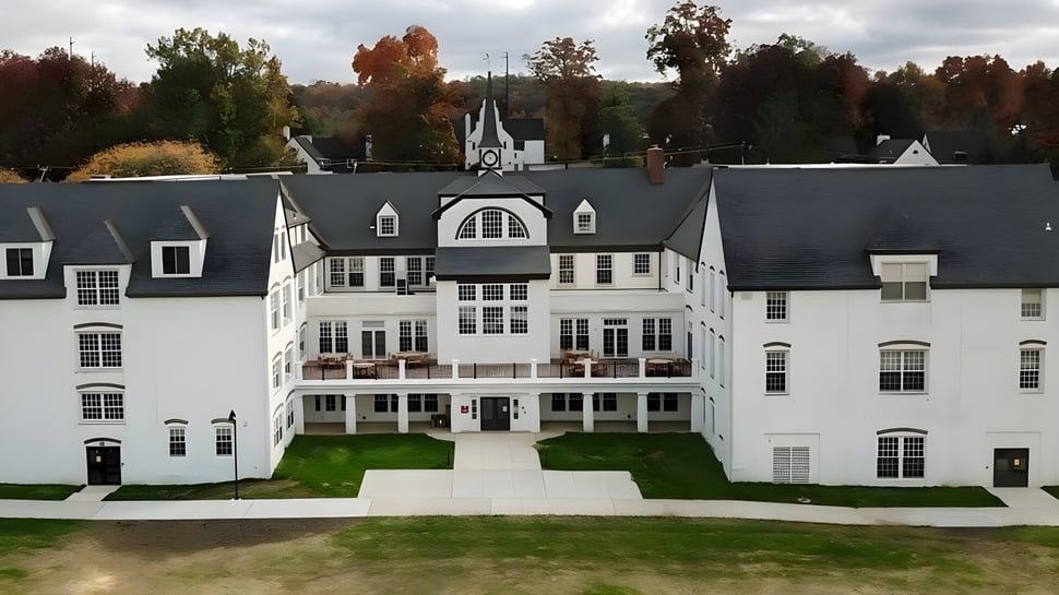 El gran edificio blanco de la Church Farm School con torre central y ventanas de arco rodeado de árboles coloridos.
