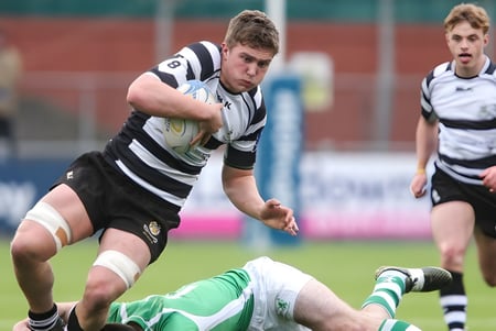 Un jugador de rugby del Cistercian College corre con el balón por el campo mientras otro jugador está en el suelo.