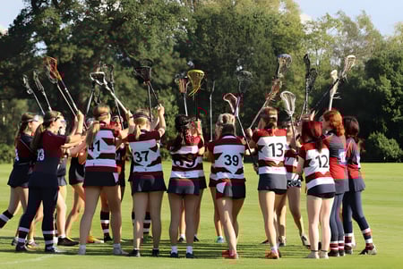 Un grupo de jóvenes deportistas está en el campo de deportes de la Claremont School con árboles al fondo.