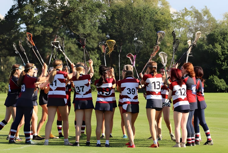 Un grupo de jóvenes deportistas está en el campo de deportes de la Claremont School con árboles al fondo.