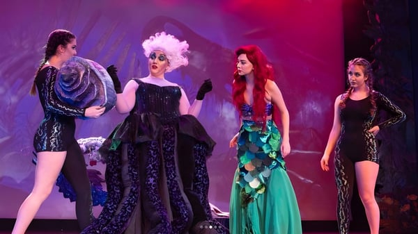 Cuatro estudiantes de la Claremont Secondary School llevan disfraces coloridos en un escenario con un fondo teatral vibrante.