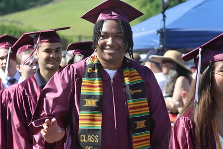 Los graduados en togas moradas de la Claremont Secondary School están frente a una carpa azul y árboles.