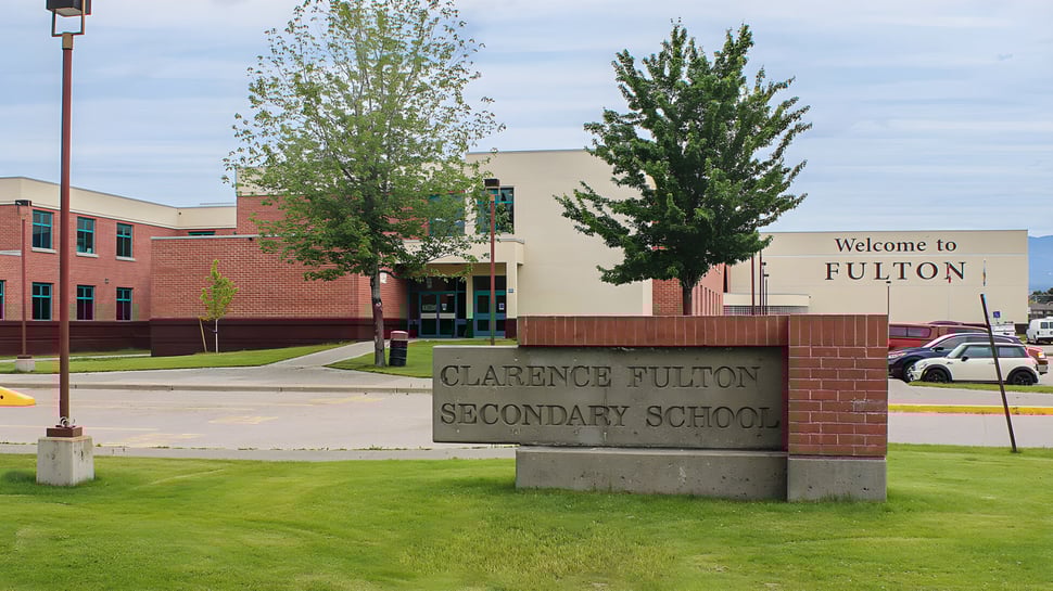 Cartel de ladrillo con la inscripción Clarence Fulton Secondary School frente al edificio escolar y árboles.