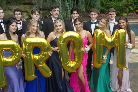 Estudiantes de la Clarence High School posan con ropa formal con grandes letras doradas frente a una piscina al aire libre.