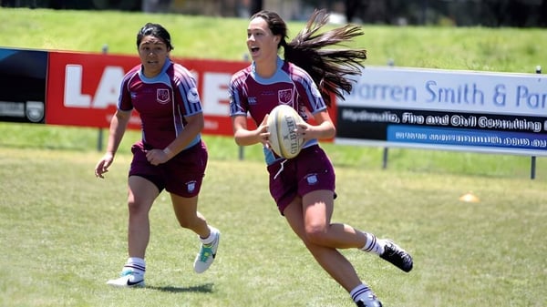 Dos jugadoras de rugby en uniforme marrón corren por el campo de la Clarence High School.