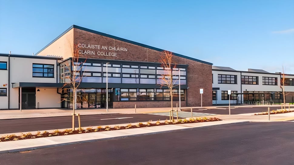 El moderno edificio de ladrillo del Clarin College con grandes ventanas y una entrada visible está rodeado de un jardín.