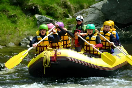 Estudiantes del Classic Plus Programm navegando un río en una balsa amarilla en un entorno verde.