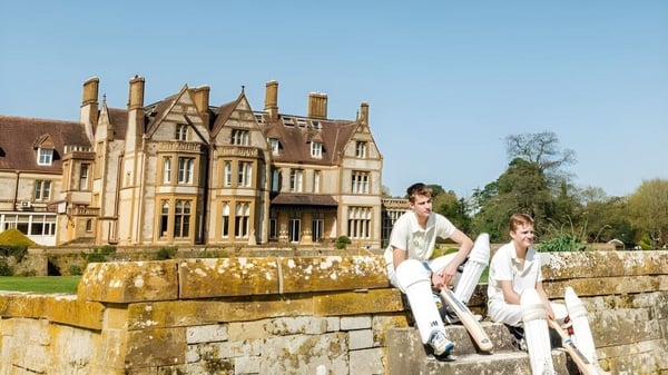 Dos personas están sentadas en un muro de piedra frente a un manor histórico en el terreno de la Clayesmore School.