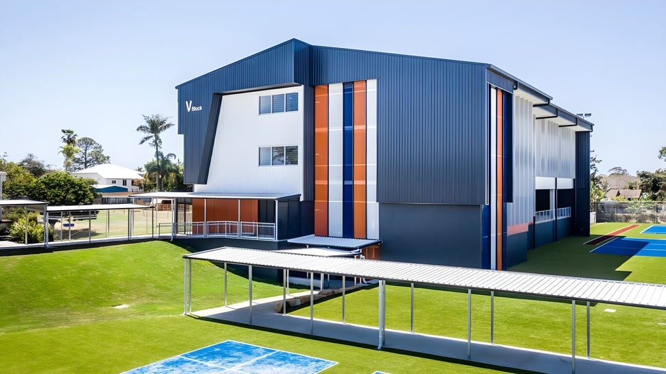El moderno edificio de varios pisos de la Cleveland District State High School con fachada azul y acentos naranjas se encuentra en un césped con palmeras.