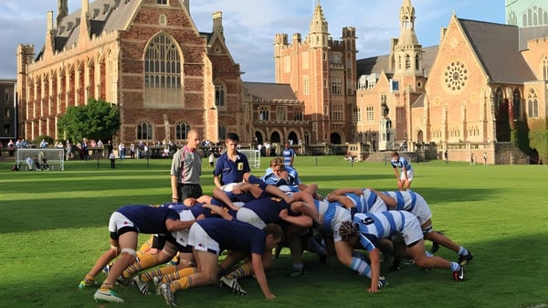 Un grupo de estudiantes en ropa deportiva forma un círculo en el campo de deportes del Clifton College frente a un edificio histórico de ladrillo.