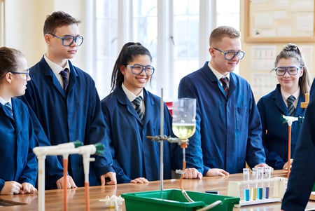 Estudiantes en togas académicas están en el laboratorio del Clifton College alrededor de una mesa con equipo científico.