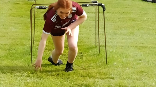 Una persona con ropa deportiva se inclina en el campo del Clonfert College frente a un paisaje cubierto de hierba.