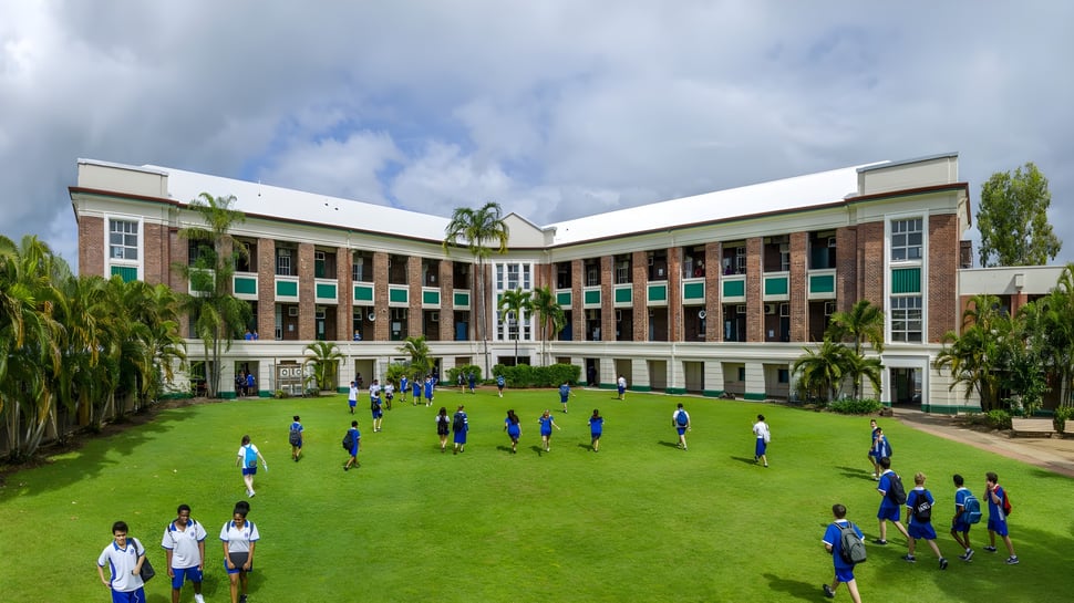 El edificio de varios pisos de la Cnoc Mhuire Secondary School con un área de césped verde y estudiantes en uniformes azules delante.