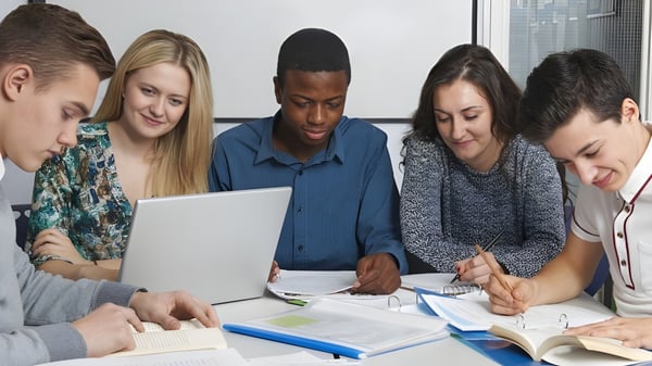Estudiantes de la Cnoc Mhuire Secondary School trabajando juntos en un proyecto con laptop y libros de texto.