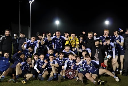El equipo deportivo de la Cnoc Mhuire Secondary School posando juntos en el campo de deportes por la noche.