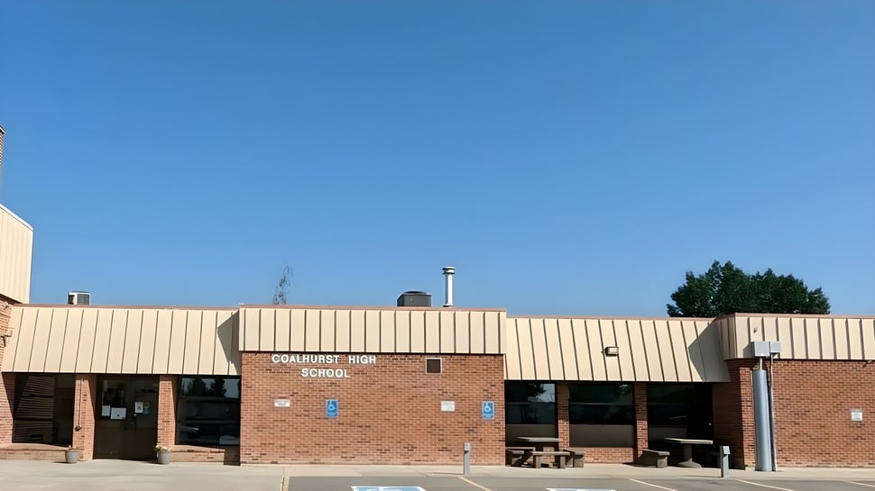 El edificio de ladrillo de Coalhurst High School está rodeado de árboles bajo un claro cielo azul.