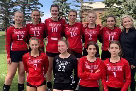 Un grupo de jóvenes estudiantes de Coalhurst High School posan juntas al aire libre en un campo con árboles de fondo.