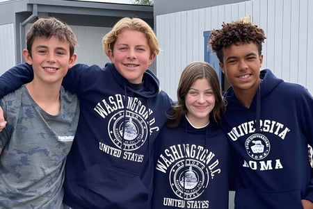 Cuatro estudiantes están frente al edificio de la Coastal Christian School y sonríen a la cámara.