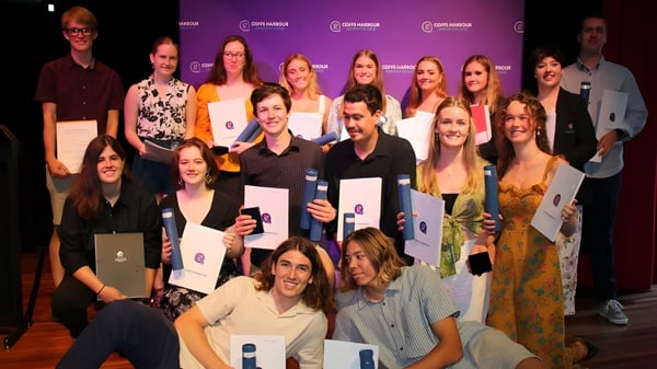 Un grupo de estudiantes del Coffs Harbour Senior College posan juntos frente a un fondo morado con el logo.