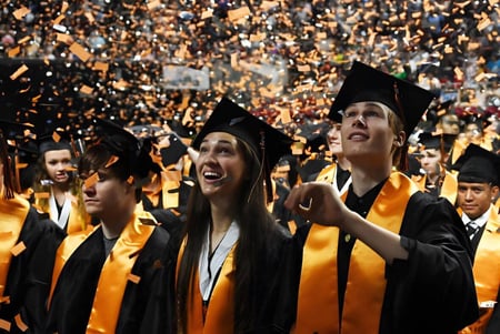 Los graduados de la Coláiste an Chreagáin celebran su graduación con togas amarillas y negras bajo confeti que cae.