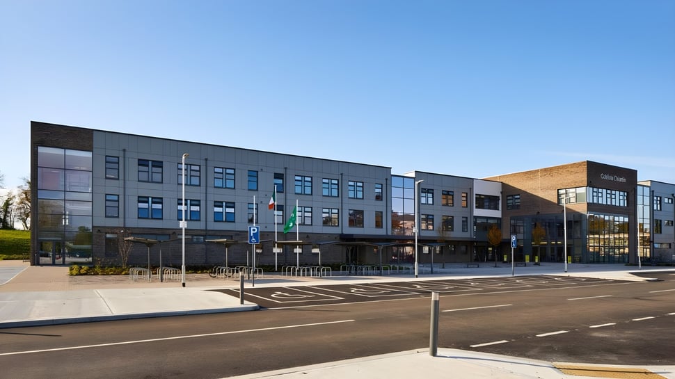 El moderno edificio de varios pisos de la Colaiste Chiarain Athlone con fachadas de vidrio y un aparcamiento bajo un cielo azul.