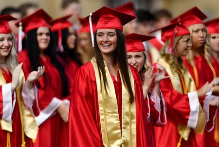Las graduadas y graduados en togas rojas y doradas están juntos en el terreno de Coláiste Chill Mhantáin.