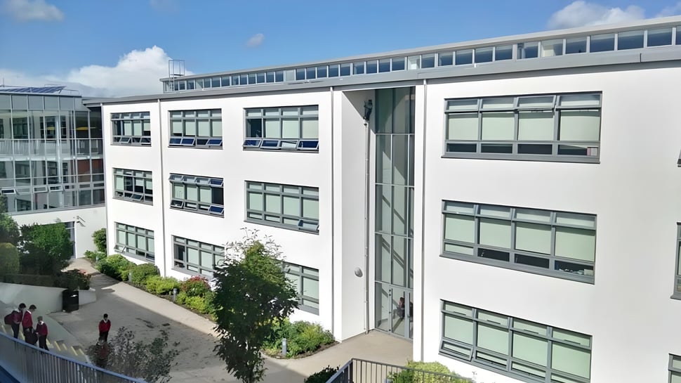 Se puede ver el edificio de varios pisos de Coláiste Chill Mhantáin con fachada de vidrio y vegetación circundante.