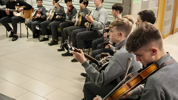 Los estudiantes tocan diferentes instrumentos musicales como guitarras y violines en la clase de música de la Coláiste Choilm.