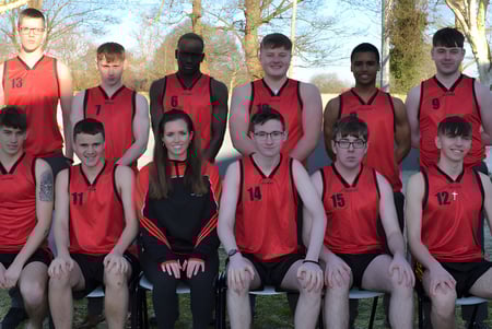 Un grupo de estudiantes de la Coláiste Éamann Rís posan al aire libre para una foto de equipo frente a árboles y césped.
